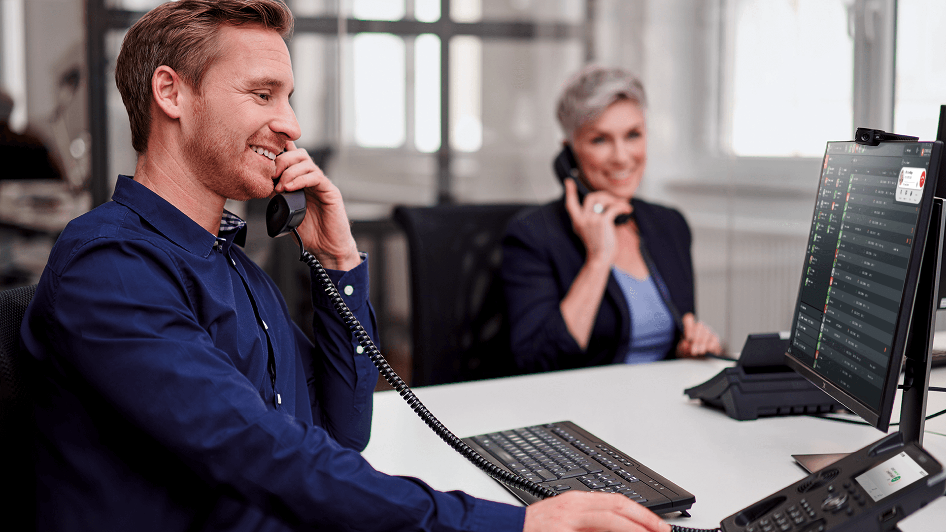 Mitarbeiter telefonieren am STARFACE Arbeitsplatz mit Tischtelefon und Bildschirm
